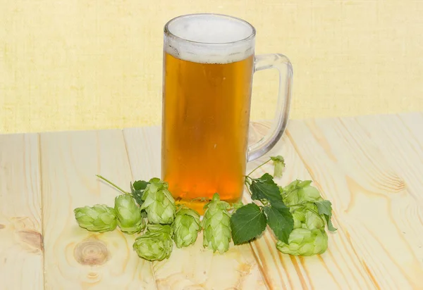 小さな木製の素朴なテーブルの上にホップコーンの間でハンドル付きの大きなガラスビールマグカップで冷たいラガービール — ストック写真