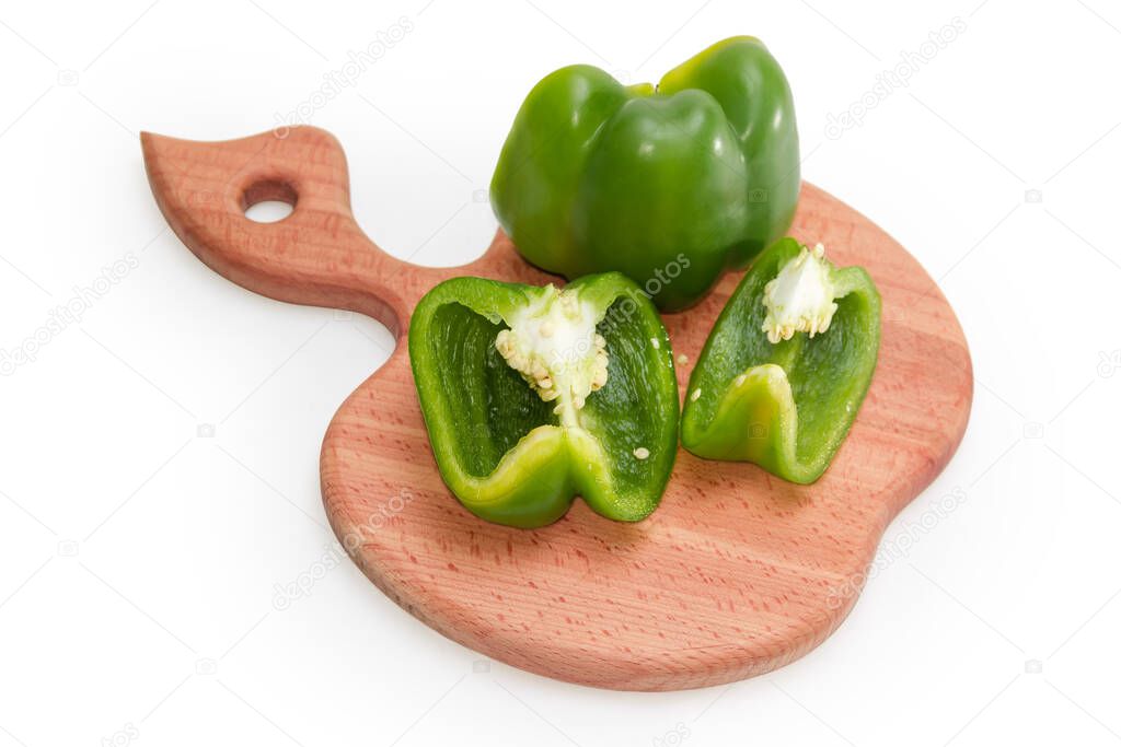 Half and slices of green bell pepper with seeds lie on the wooden cutting board in the shape of an apple on a white background, selective focus
