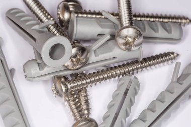 Pile of cross recessed pan head tapper screws with silvery corrosion coating and appropriate plastic split-ribbed anchors, close-up in selective focus clipart