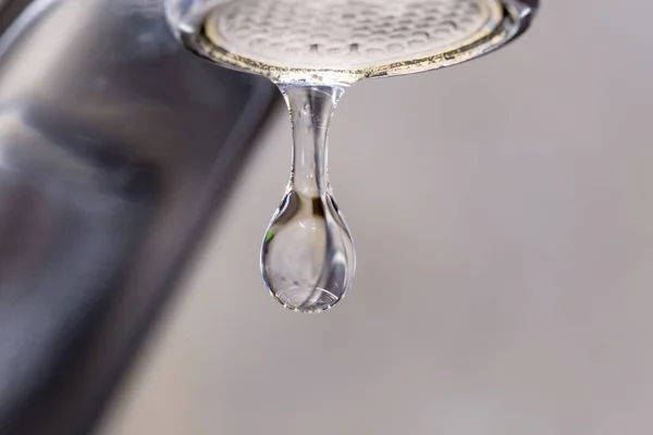 Drop of water from the leaking faucet. Fragment of tap outlet with aerator on a blurred background, close-up in selective focus