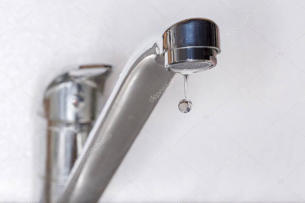 Drop of water from the outlet with aerator of leaking mixer faucet on a blurred background, close-up in selective focus