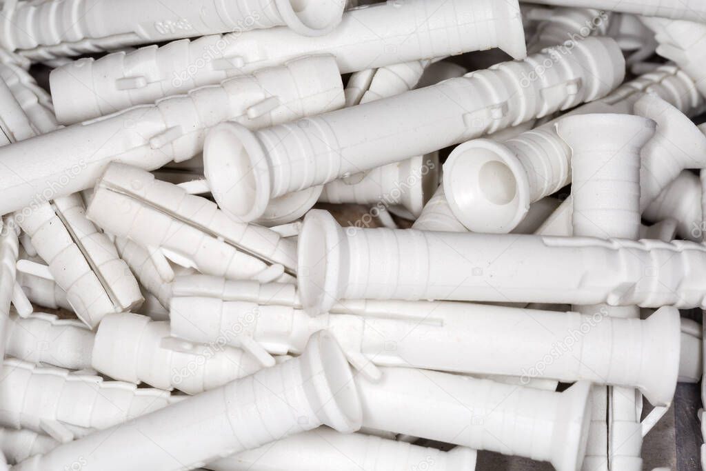 Pile of white plastic split-ribbed anchors with size marking, top view close-up in selective focus