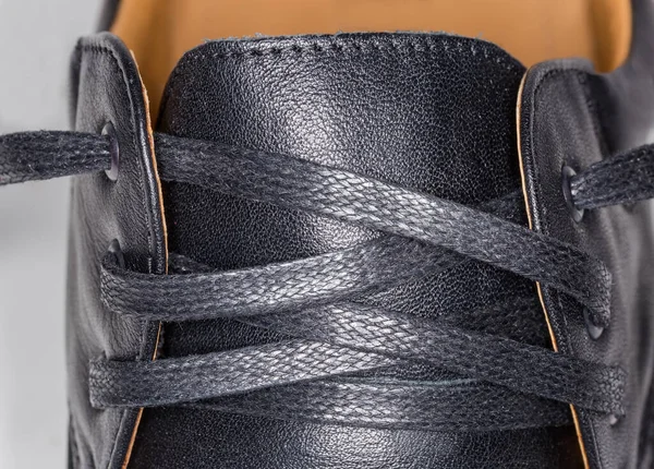 Untied shoe lacing traditional criss cross method with flat shoelace, fragment of the men's black leather low shoe close-up