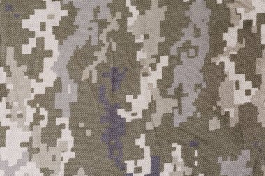 Pikselleştirilmiş dijital kamuflaj desenli, hafif buruşuk bir kumaş parçası. Zeytin yeşili ve gri yakın plan. Arkaplan, doku