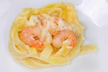 Erişteler yuvaya doluşmuş ve beyaz tabakta karides ve beyaz sosla pişirilmiş, seçici odak noktasında yakın plan.