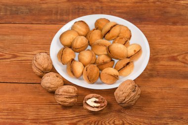 Fındık şeklinde kurabiyeler, beyaz tabakta yoğunlaştırılmış sütlü karamel ve ahşap bir masada ön planda gerçek ceviz.