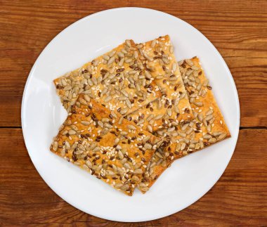 Düz dikdörtgen çıtır kurabiyeler, poğaça ile yapılır, susam, keten ve ayçekirdeği serpiştirilir eski bir kırsal masada beyaz tabakta, üst manzara