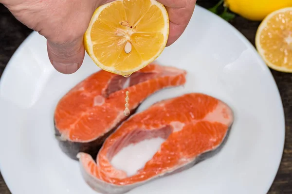 Lemon half in hand during juice squeezing on to the trout pieces for their preparation, close-up in selective focus