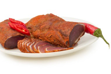 İki parça kurutulmuş domuz filetosu, beyaz arka planda beyaz bir tabakta kırmızı biber, seçici odak noktasında yakın plan.