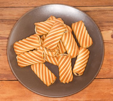 Çerezler flüt tüpleri şeklinde, kahverengi bir tabakta reçel dolgulu, kırsal bir masada, en üstte yakın plan.