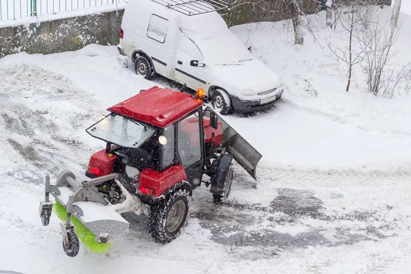 小红轮式拖拉机 前排雪犁 后排旋转扫帚 下雪天工作时在住宅区院子里 — 图库照片