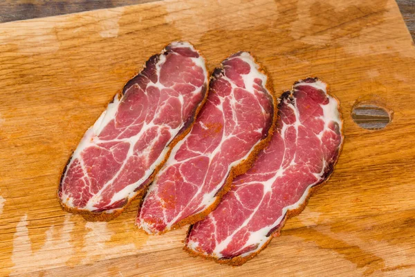Slices of dry-cured pork neck on a wooden cutting board close-up