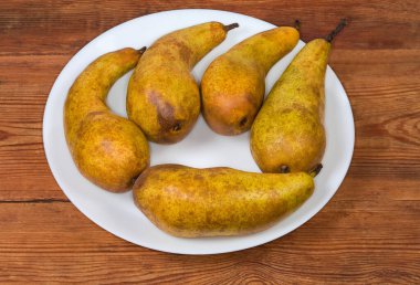 Konferansın olgun armutları. Eski bir kırsal masada beyaz bir tabakta kahverengi renkli çeşitli sarılar.