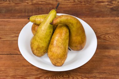 Konferansın olgun sarı ve kahverengi armutları eski bir kırsal masada beyaz bir tabakta çeşitlilik gösteriyor.