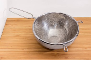 Boş paslanmaz çelik elek, paslanmaz çelik kasede tel örgü beyaz arka planda ahşap bir yüzey, seçici odak noktasında yakın plan