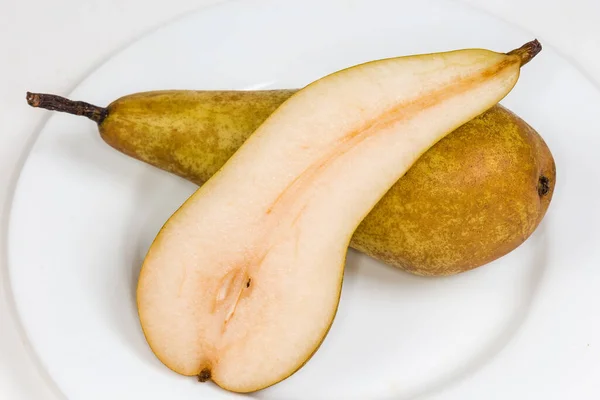 カンファレンス品種の熟した黄色の梨の半分は 白いプレート上の同じ全体の梨の上にあり トップビューのクローズアップ — ストック写真