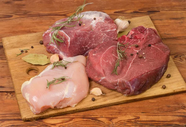 様々な調理されていない骨のない肉の大きな作品 皮のない鶏の胸肉 豚肉と古い素朴なテーブルの上に木製のまな板の上に異なるスパイスと後ろ足の牛肉 — ストック写真