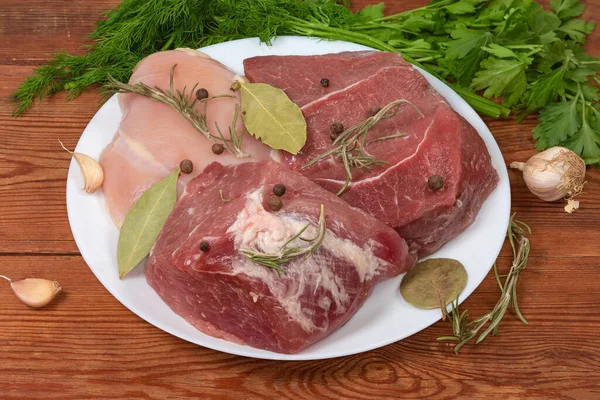 白い皿の上の鶏の胸肉 骨なしの豚肉と牛肉の大きな作品 スパイスと古い素朴なテーブルの上の緑 — ストック写真