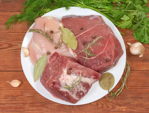 古い素朴なテーブルのスパイスや緑の間で白い皿の上に鶏の胸肉 骨のない豚肉と牛肉の大きな作品 トップビュー — ストック写真
