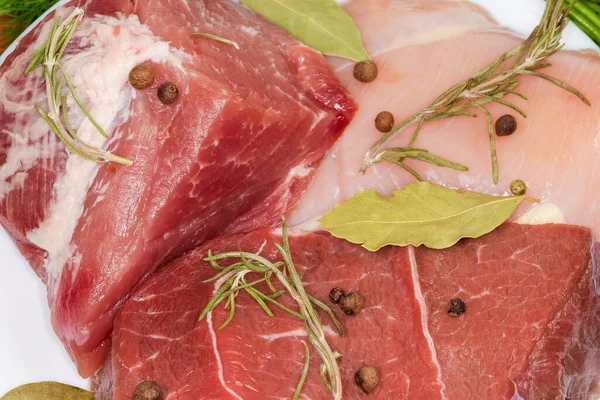 Pieces of uncooked beef, pork and chicken with some spices, top view close-up