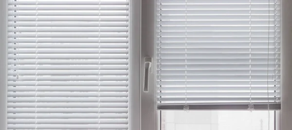 Part of a modern plastic window with partly raised white Venetian blinds and mosquito net, panoramic inside view