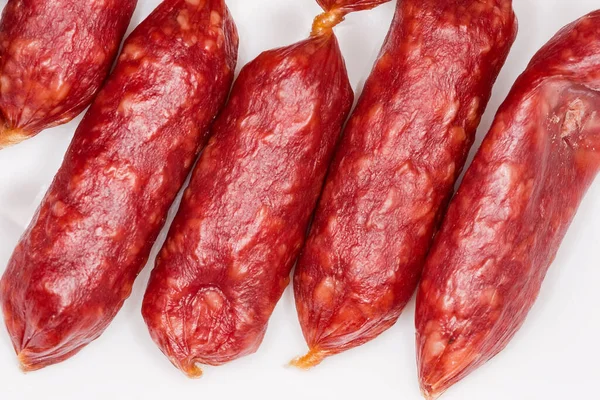 Small thin dry cured sausages in natural casing on a white surface close-up, fragment top view