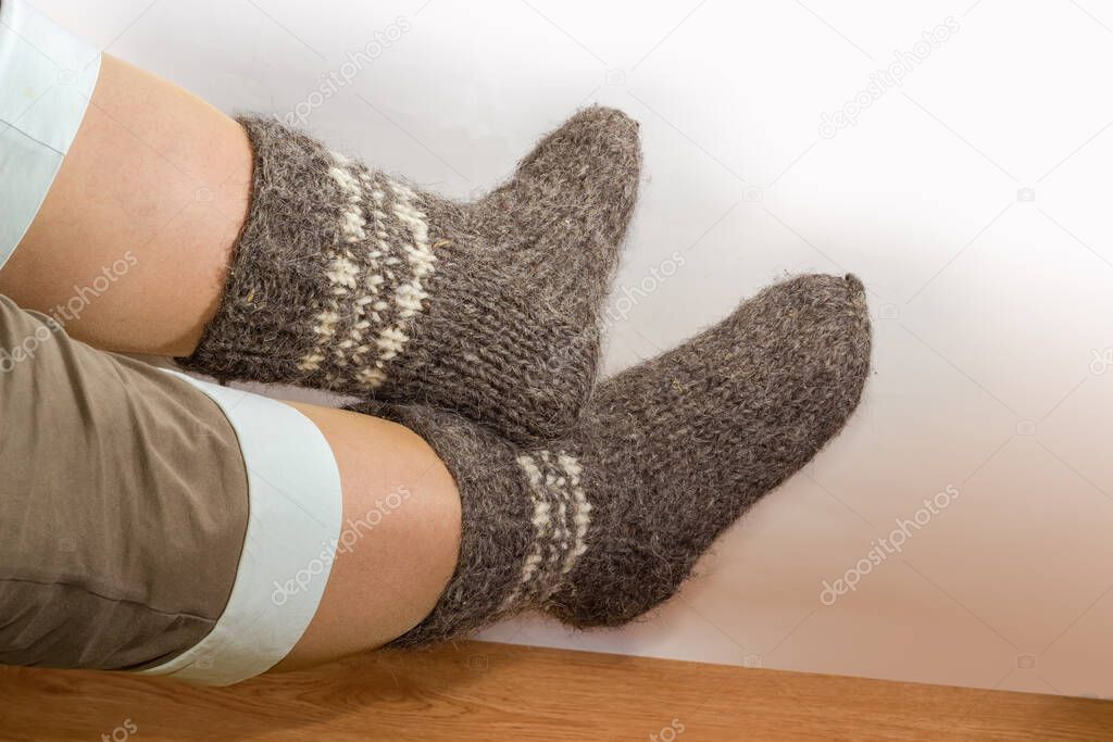 Pair of the thick gray wool hand-knitted socks on women legs against the wooden floor and light wall