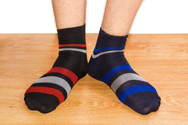 Pair of black socks with different color of the ornament on the men foots on a wooden floor against a white background