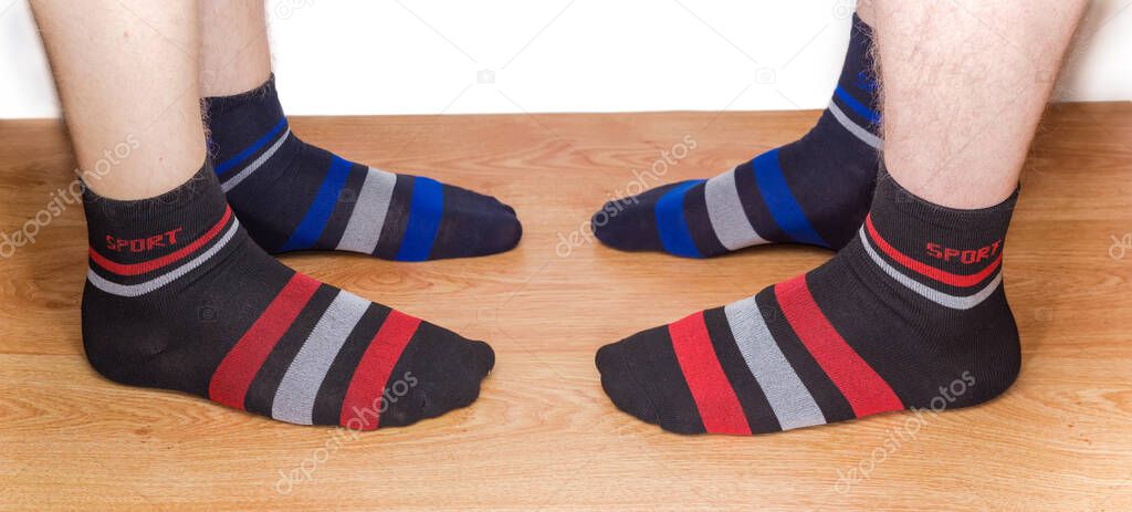 Black socks with different color of the ornament on the two mens legs on a wooden floor against a light background