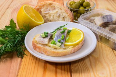 Salamura Atlantik ringa filetosundan yapılmış açık sandviç, beyaz ekmek, tereyağı, taze limon ve doğranmış yeşil tabakta malzemelere karşı, seçici bir odak noktasında yakın plan