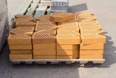 Sarı delikli dekoratif yüz tuğlaları, eğimli tek açı, açık hava deposundaki ahşap paletin üzerine istiflenmiş.