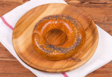 Pişmeden önce haşlanmış haşhaş tohumları serpiştirilmiş geleneksel Doğu Avrupa halka şeklinde ekmek rulosu eski bir kırsal masada ahşap bir tabakta uzanır.