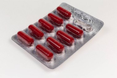 Açık renkli bir yüzeyde, koyu kırmızı kapsüller şeklinde kullanılan tek bir kapsül, seçici odak noktasında yakın çekim.