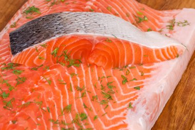 Dilimlenmemiş çiğ somon balığı, somon filetosu üzerine serpiştirilmiş deriyle ahşap kesme tahtasına serpiştirilmiş, seçici odak noktasında yakın plan.