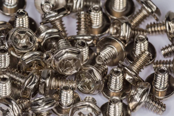Pile of cylindrical self-threading sheet metal screws  with combined hex and cross recessed head and white and anti corrosion coating, fragment close-up in selective focus, background