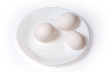 Beyaz tabakta, arka planda üç tane çiğ tavuk yumurtası.