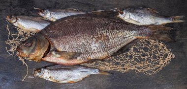Salted and air-dried big bream and several roach fish on a black surface with part of fishing net