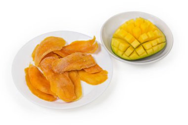 Dried slices of mango pulp on white dish against a fresh mango cut in form the hedgehog style on saucer on a white background