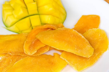 Dried slices of mango pulp against the fresh cut mango half, close-up in selective focus