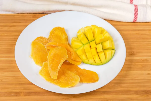 Dried slices of mango pulp and fresh mango half cut in form the hedgehog style on white dish on a wooden surface