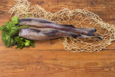 Kırsal bir masada maydanozlu kafasız ve balık ağlı iki çiğ kırmızı hake leşi.
