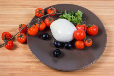 Siyah zeytinlerin, kiraz domateslerinin ve ahşap yüzeyde maydanozun arasına batırılmış taze mozzarella peyniri topu.