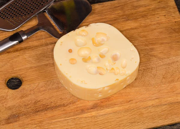 Piece of Swiss-type cheese on a wooden cutting board against the cheese slicer and cheese grater