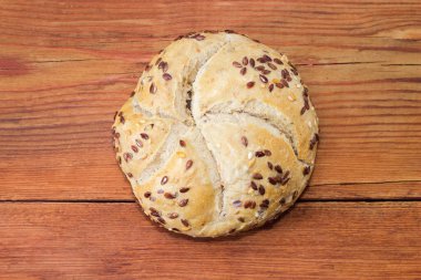 Yuvarlak buğday ekmeği, keten ve susam tohumları serpiştirilmeden önce eski bir kırsal masada uzanır, üst manzara