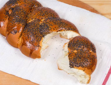 Pişmeden önce haşhaş tohumu serpiştirilmiş tatlı örülmüş ekmek ve tekstil peçetesinin bir parçası, üst manzara.