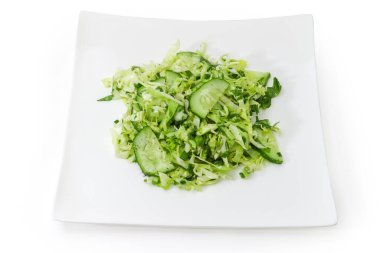 Dilimlenmiş taze lahana, salatalık ve doğranmış yeşil soğandan yapılmış sebze salatası beyaz arka plandaki kare beyaz tabakta.