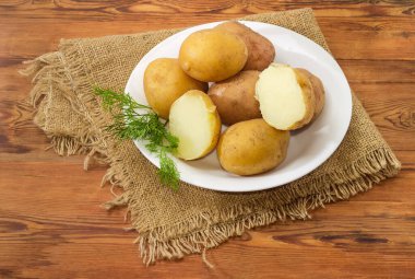Potatoes boiled in their skins with dill twig on the white dish on an old rustic table with sackcloth clipart