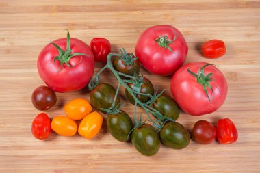 Dalda taze, taze, olgun domatesler ve ayrı ayrı, ahşap kesme tahtasındaki sıradan pembe domatesler.