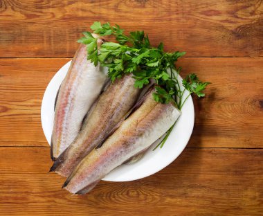 Alaska pollock 'unun çözülmemiş cesetleri, başsız, kuyruksuz ve eski bir kırsal masada taze maydanozsuz.