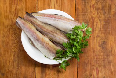 Alaska pollock 'unun çözülmemiş cesetleri, başsız, kuyruksuz ve eski bir kırsal masada taze maydanozsuz.